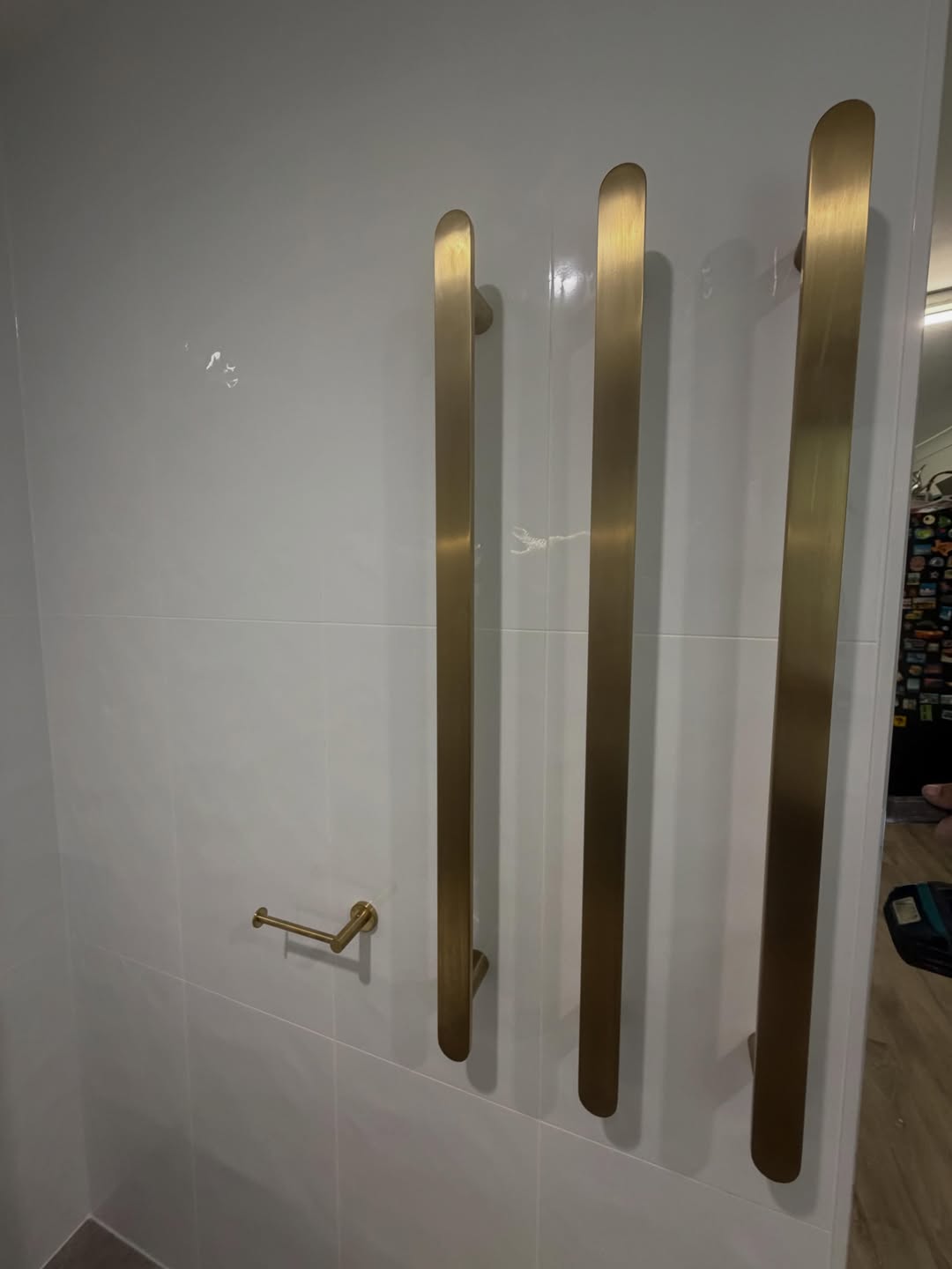 Close-up of three brass vertical towel bars and a brass toilet roll holder