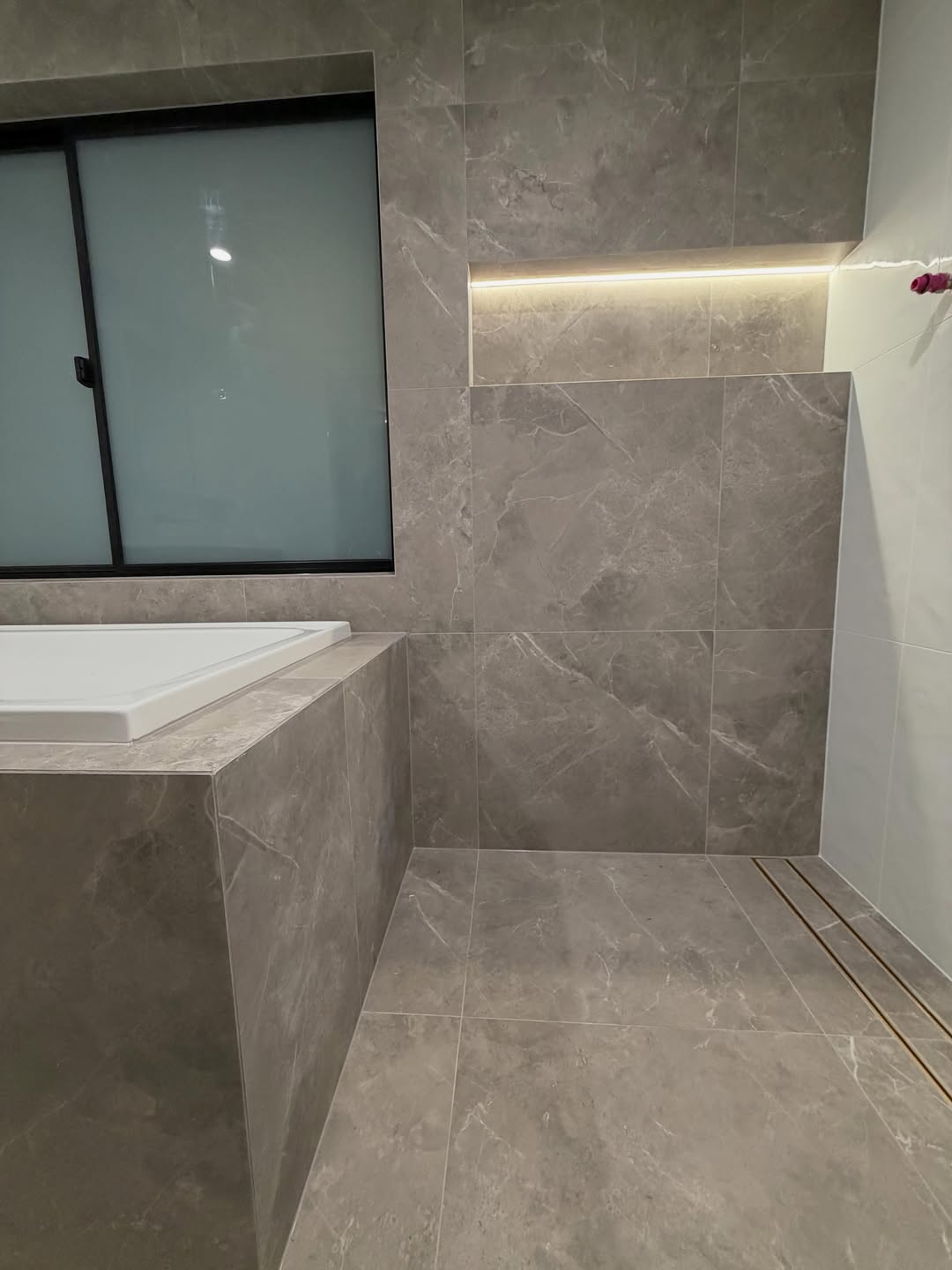 Marble-look tiled bath alcove with backlit niche and window