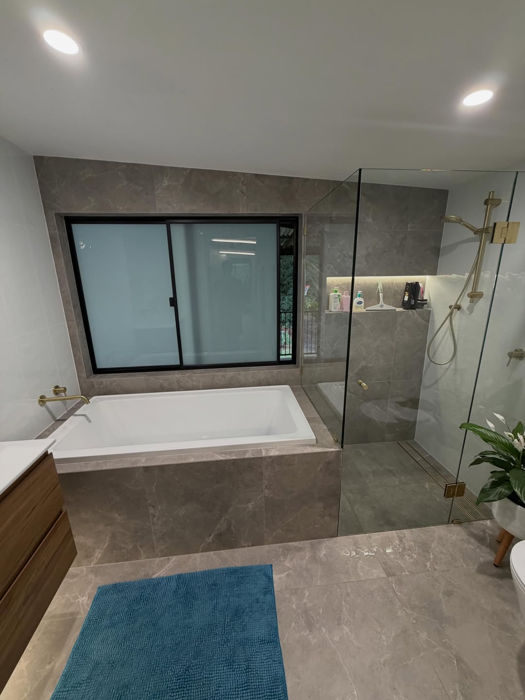 Freestanding bath and glass-walled shower with brass rain shower head