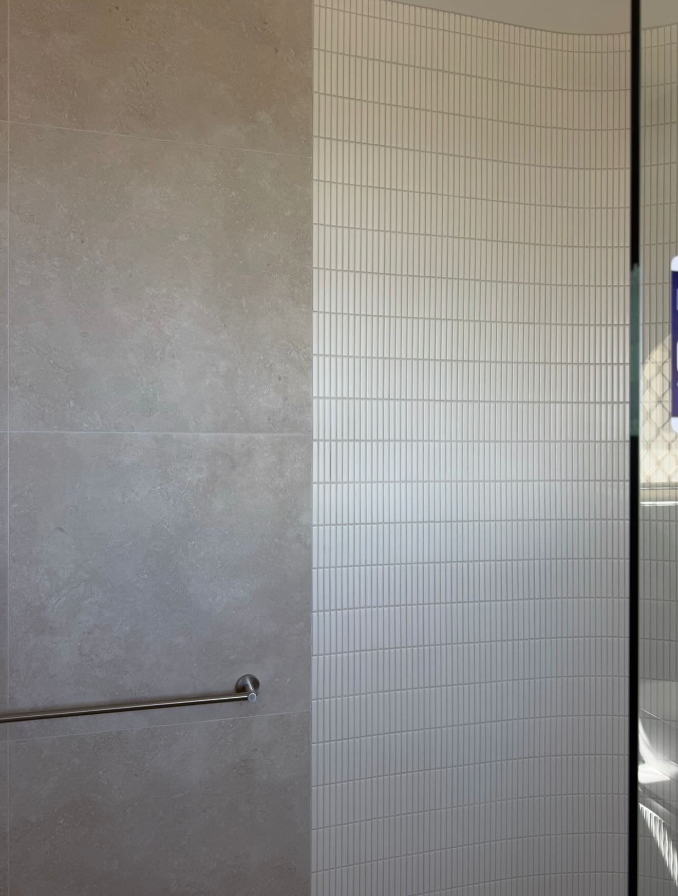 Close-up of a curved tiled wall meeting a frameless glass shower screen