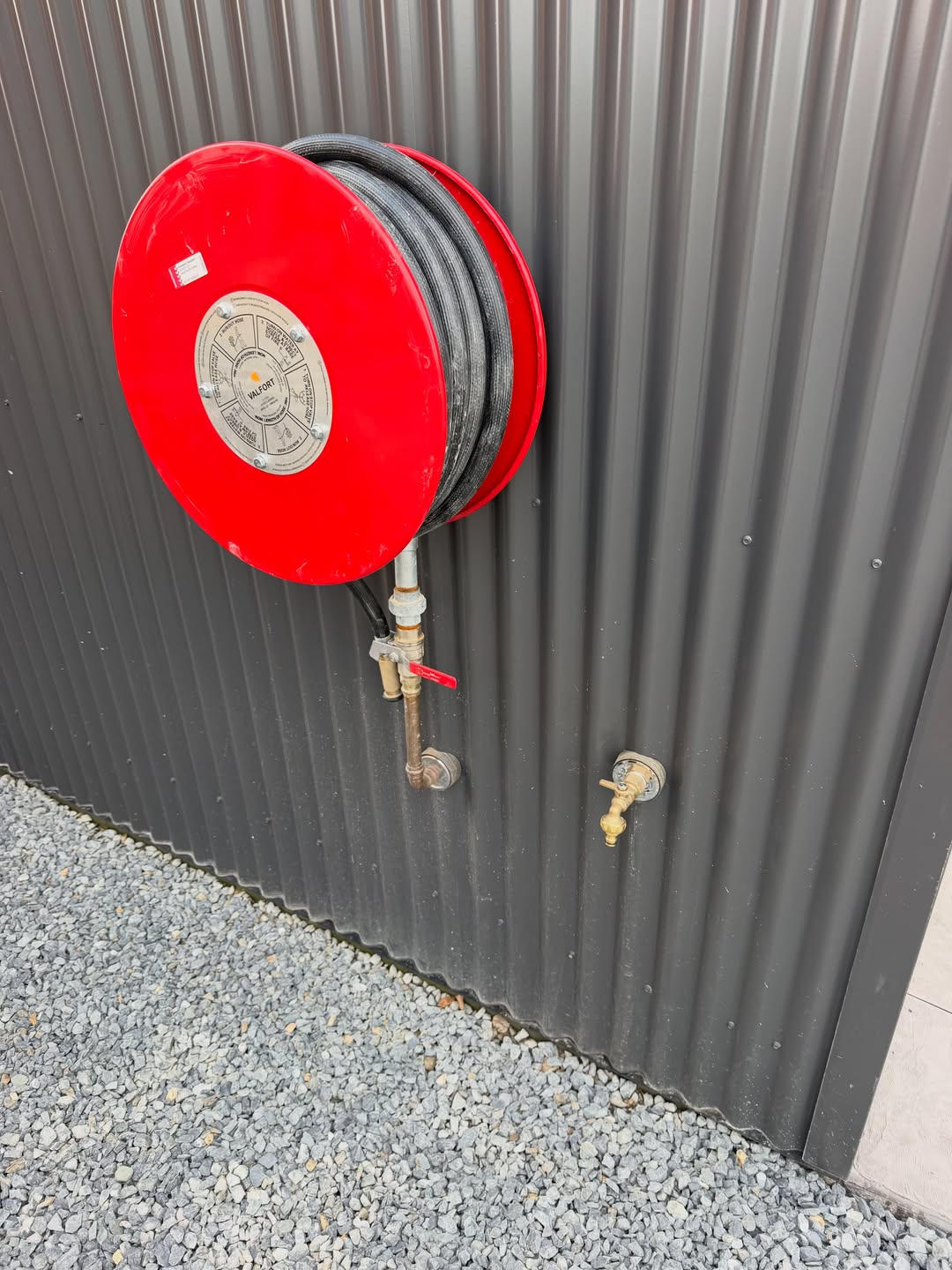 Red fire hose reel mounted on the exterior wall of the commercial shed