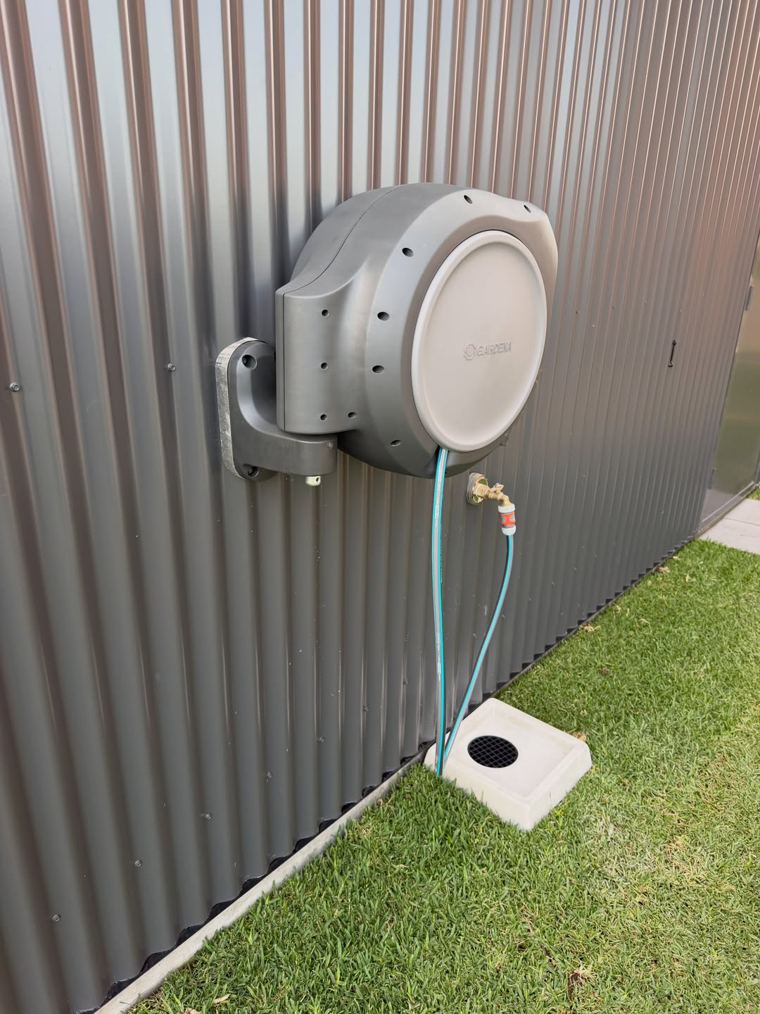 Grey retractable garden hose reel mounted on the shed exterior