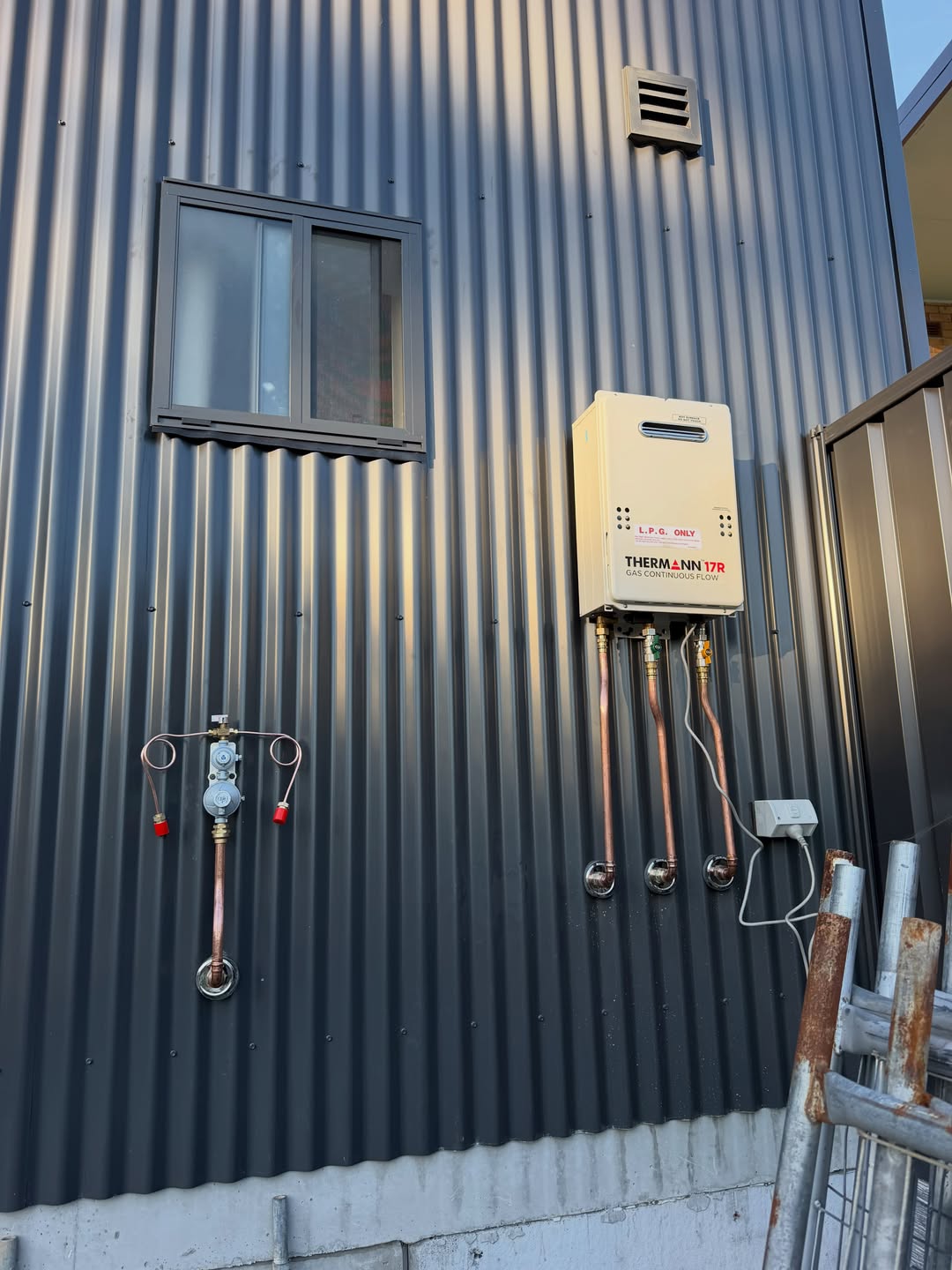 Commercial LPG continuous-flow hot water unit with copper pipework on a shed exterior