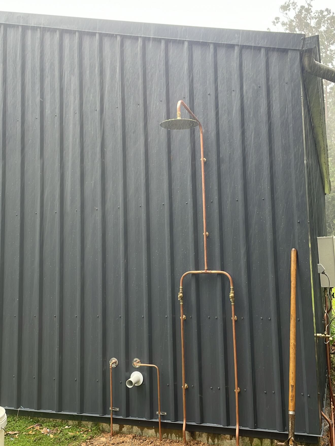 Copper outdoor shower fitting mounted on a rural property shed wall