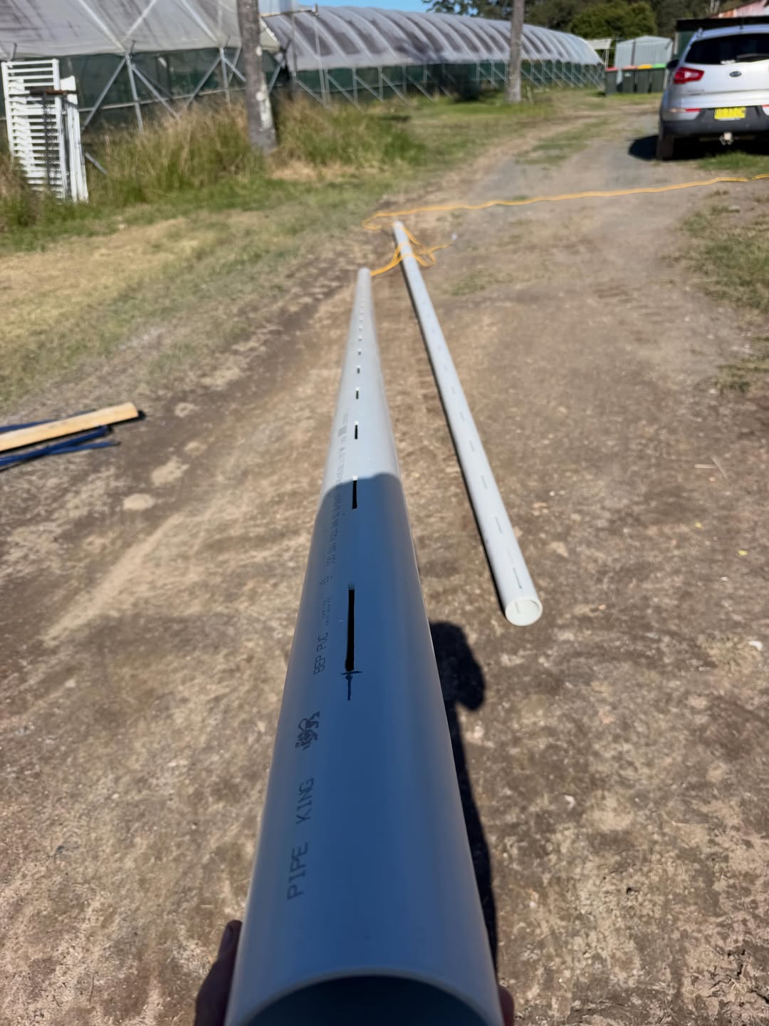 Lengths of slotted 100mm PVC pipe laid out on a rural driveway at Lowanna, ready for installation