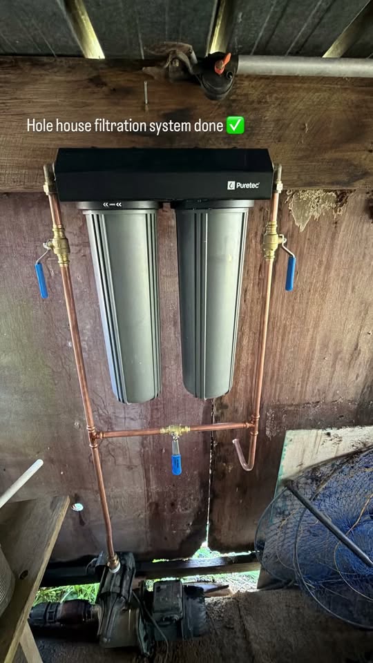 Puretec dual-cartridge whole-house water filtration system with copper pipework and isolation valves, mounted under a shed roof