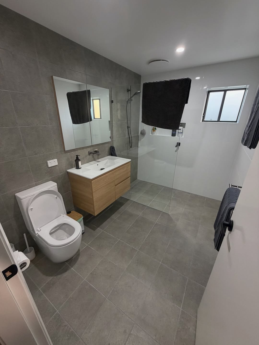 Finished bathroom with floating oak vanity, walk-in shower and toilet